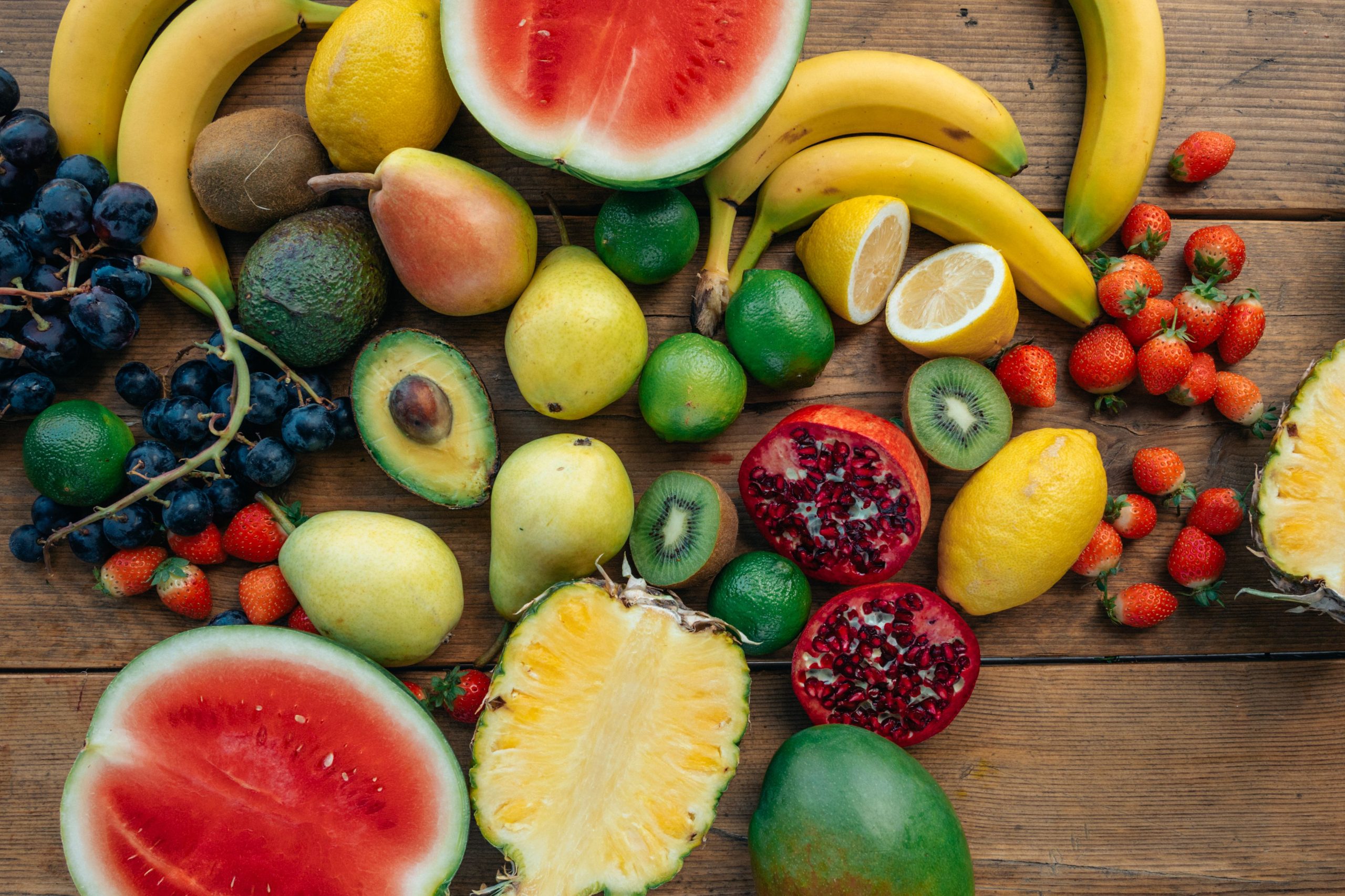Colorful variety of fresh fruits including watermelon, pineapple, and grapes on a wooden surface.